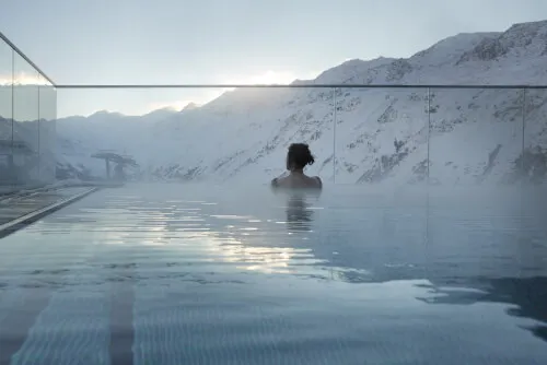 Frau schwimmt im Außenpool des TOP Hotel Hochgurgl mit schneebedeckten Bergen im Hintergrund