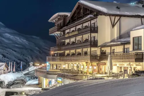 TOP Hotel Hochgurgl bei Nacht, umgeben von Schnee, mit Autos im Vordergrund und Flaggen.