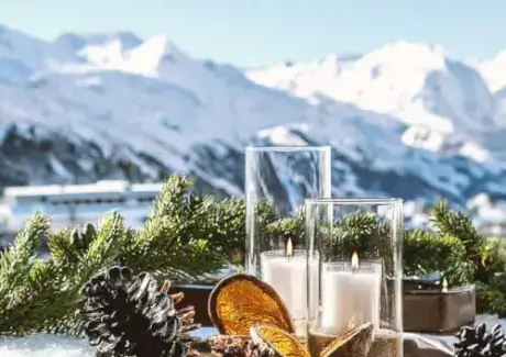 A winter decoration scene at TOP Hotel Hochgurgl with candles, pine cones, and a snowy mountain view.