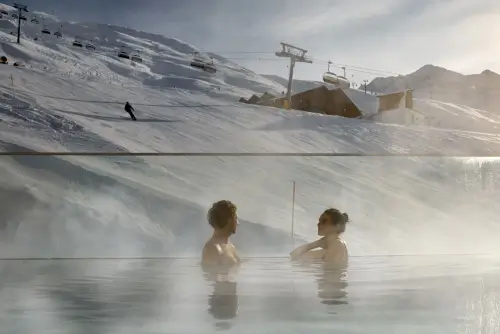 Zwei Personen im beheizten Pool mit Blick auf die schneebedeckten Berge und Skilifte.