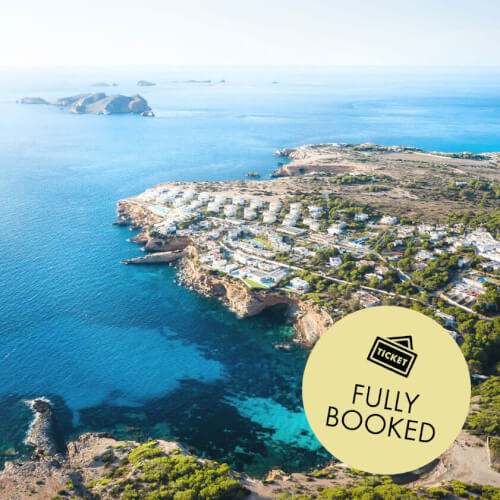 Aerial view of the scenic Ibiza coast with crystalline waters, promoting the 7Pines Resort event with beats by DJ Sergio Mussa, local cuisine, and a raffle