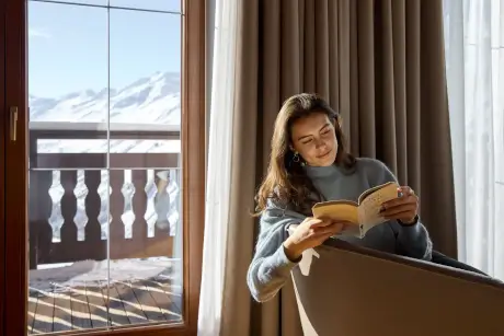 Eine Frau, die am Fenster im TOP Hotel Hochgurgl mit atemberaubendem Bergblick liest.