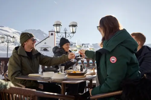 Freunde stoßen mit Getränken auf einer sonnigen Terrasse im TOP Hotel Hochgurgl an, umgeben von atemberaubenden Bergen.