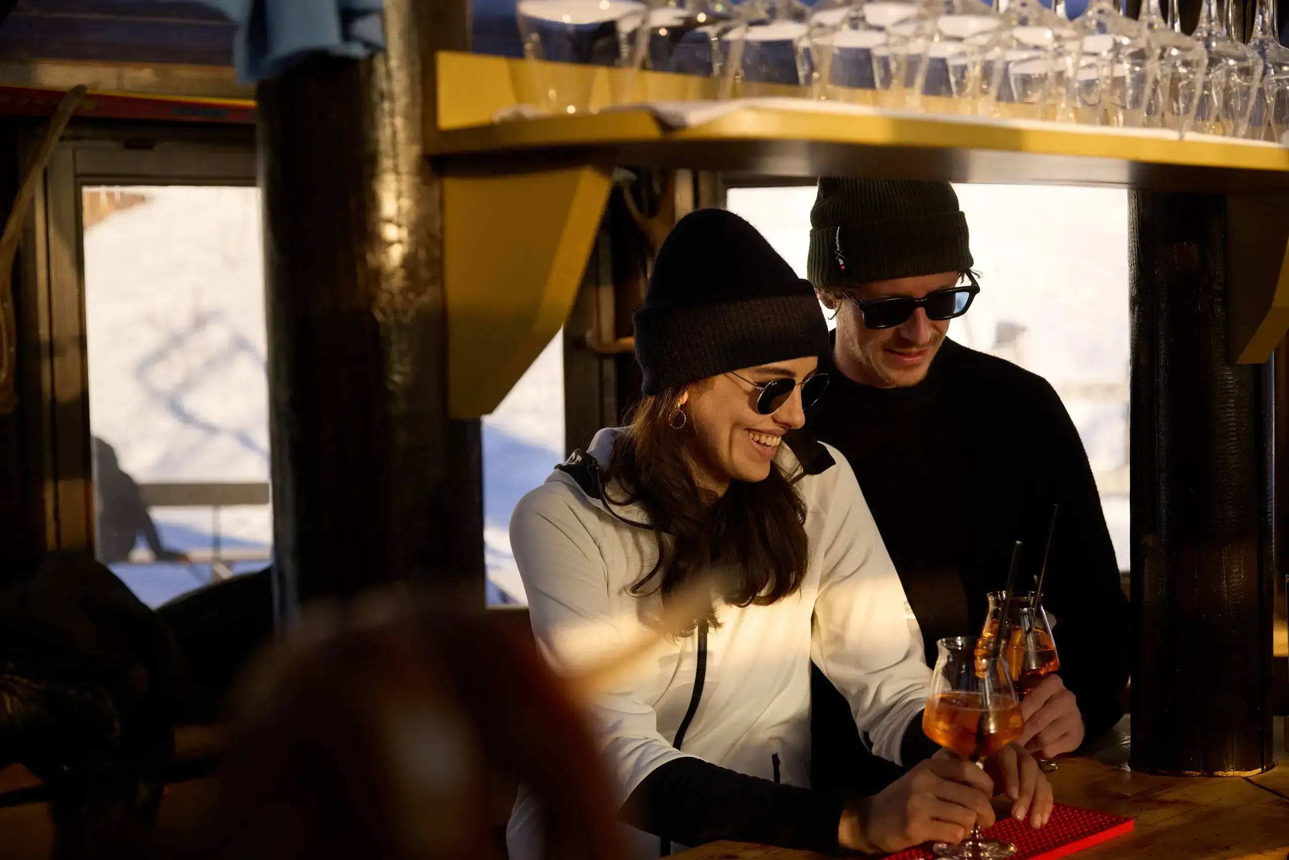 Smiling couple in winter clothing enjoys drinks at the bar at TOP Hotel Hochgurgl.