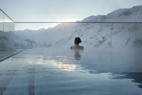 Gast entspannt im Außenpool des TOP Hotel Hochgurgl mit schneebedeckten Bergen im Hintergrund.