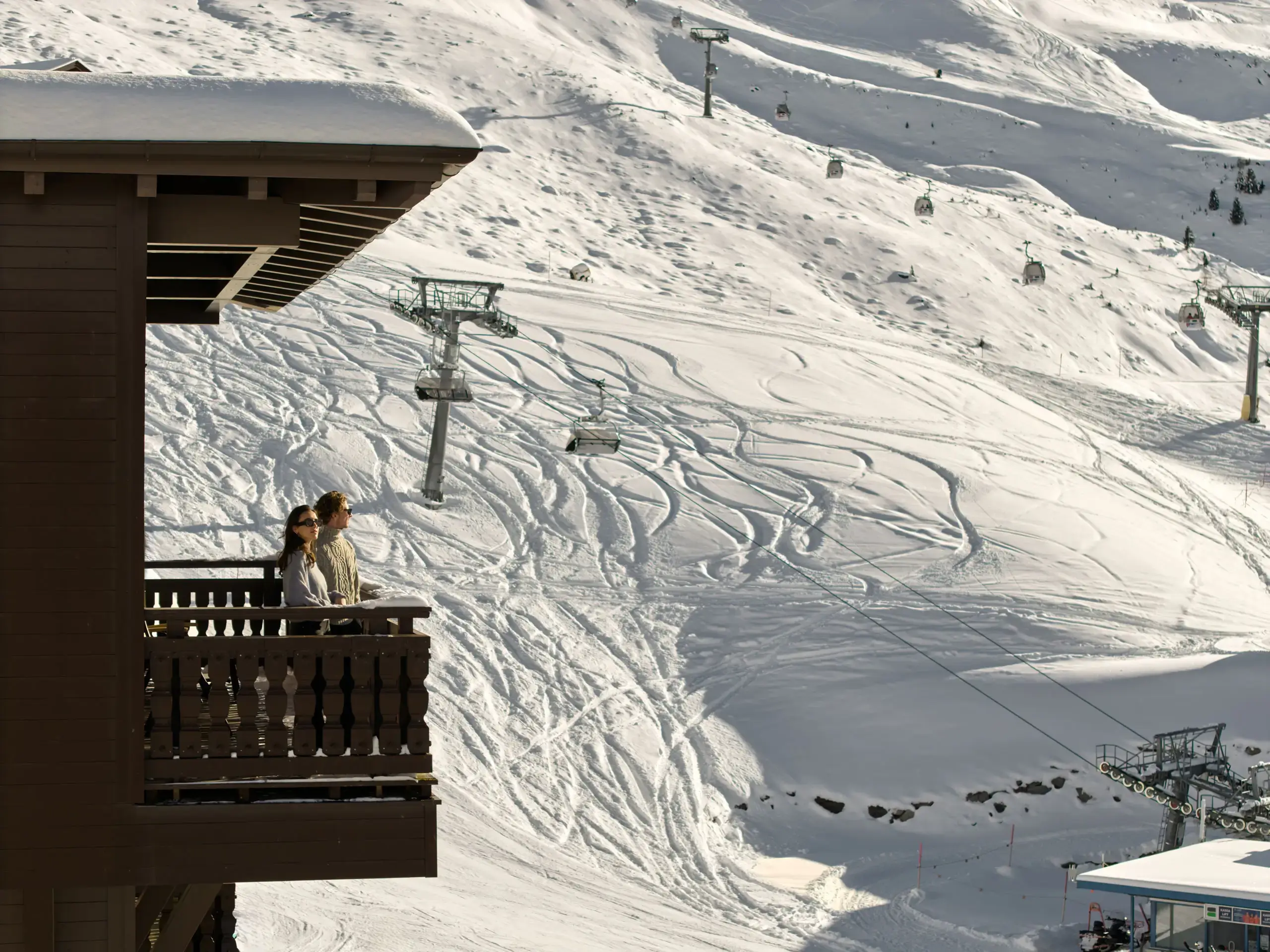 Zwei Gäste auf einem Hotelbalkon mit Blick auf verschneite Skipisten und Skilifte in Hochgurgl.