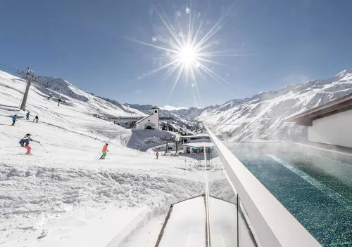 Skifahrer auf der Piste neben dem Infinity-Pool des TOP Hotel Hochgurgl mit Bergpanorama.