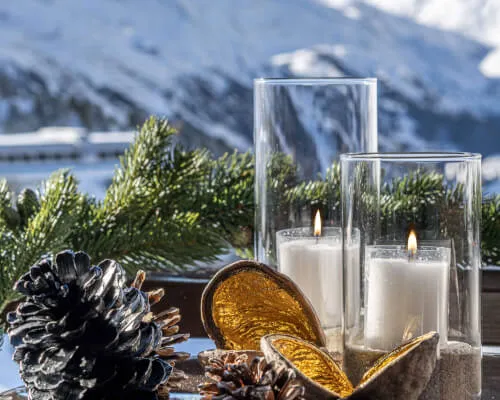 Gemütliche Winteratmosphäre mit Kerzen, Pinienzapfen und schneebedeckten Bergen.