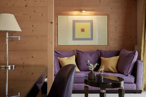 Elegant interior of Promontoria Hochgurgl GmbH hotel room with purple couch, yellow pillows, and glass table