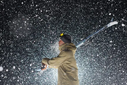 Nacht-Skiläufer mit Skiern im Schneesturm unter Flutlicht.