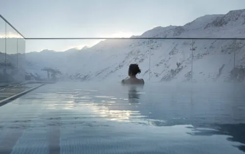 Person entspannt im Außenpool mit Blick auf die schneebedeckten Berge im TOP Hotel Hochgurgl.