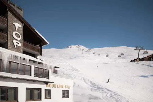 Das TOP Hotel Hochgurgl umgeben von verschneiten Pisten mit einem Skilift und einem Skifahrer bei der Abfahrt, unter einem klaren Himmel - MOUNTAIN SPA.
