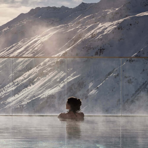 Frau schwimmt im Pool mit Blick auf verschneite Berge, nahe TOP Hotel Hochgurgl