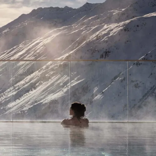 Frau beim Schwimmen in einem Pool mit Blick auf verschneite Berge, in der Nähe des Promontoria Hochgurgl GmbH - TOP Hotel Hochgurgl
