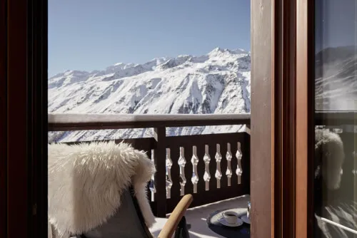 A chair on a balcony overlooking a snowy mountain range, with no text or specific details visible